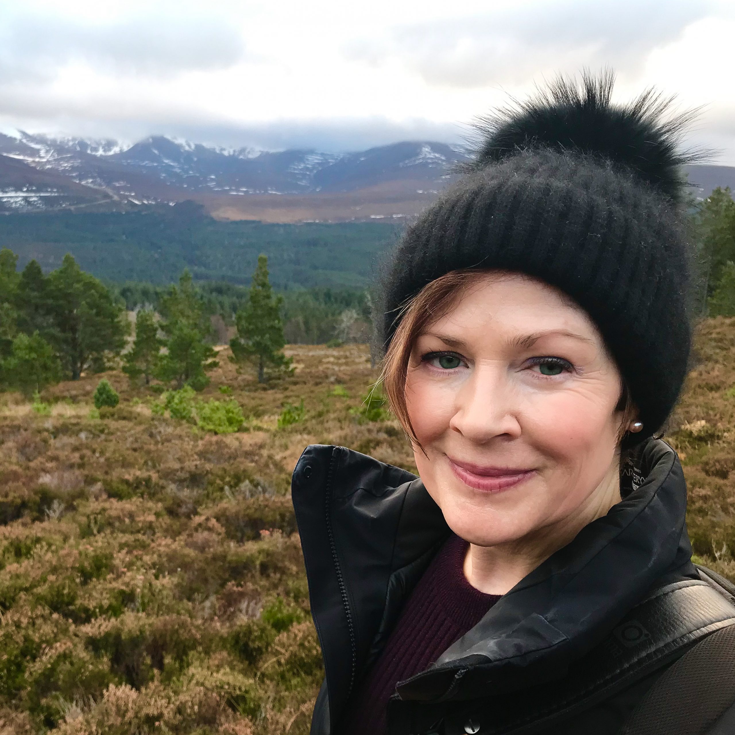 A photo of author Lynne Heasley wearing winter gear in front of a large field and mountains.